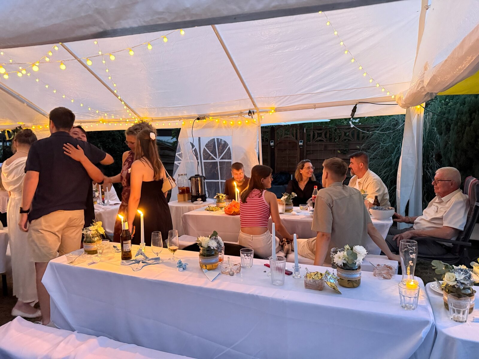Guests celebrating beneath the reception marquee and glowing string lights at dusk